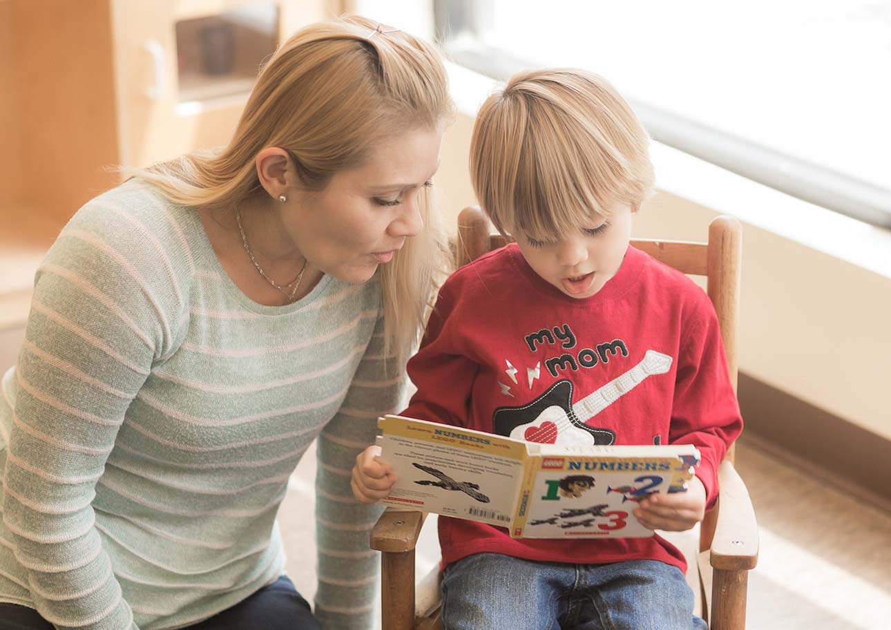 A photo of a little boy reading a book to his mom.